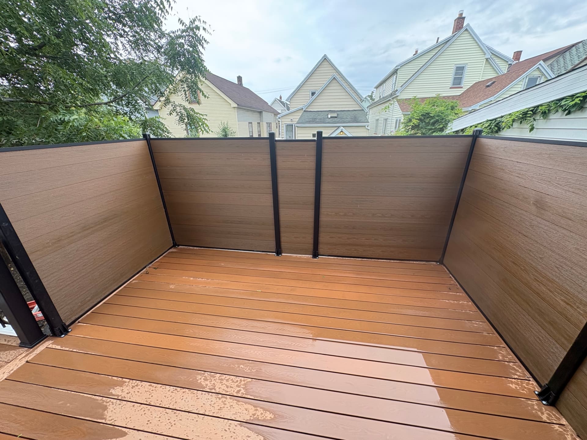 Composite deck with wood-tone privacy panels and black aluminum posts on a back porch