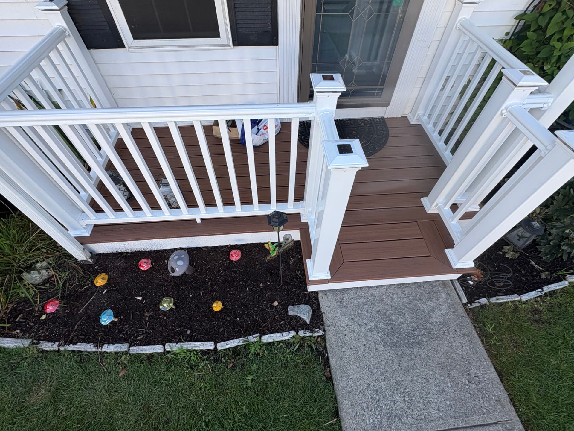 Overhead view of a rebuilt front porch with brown composite boards and white vinyl railing
